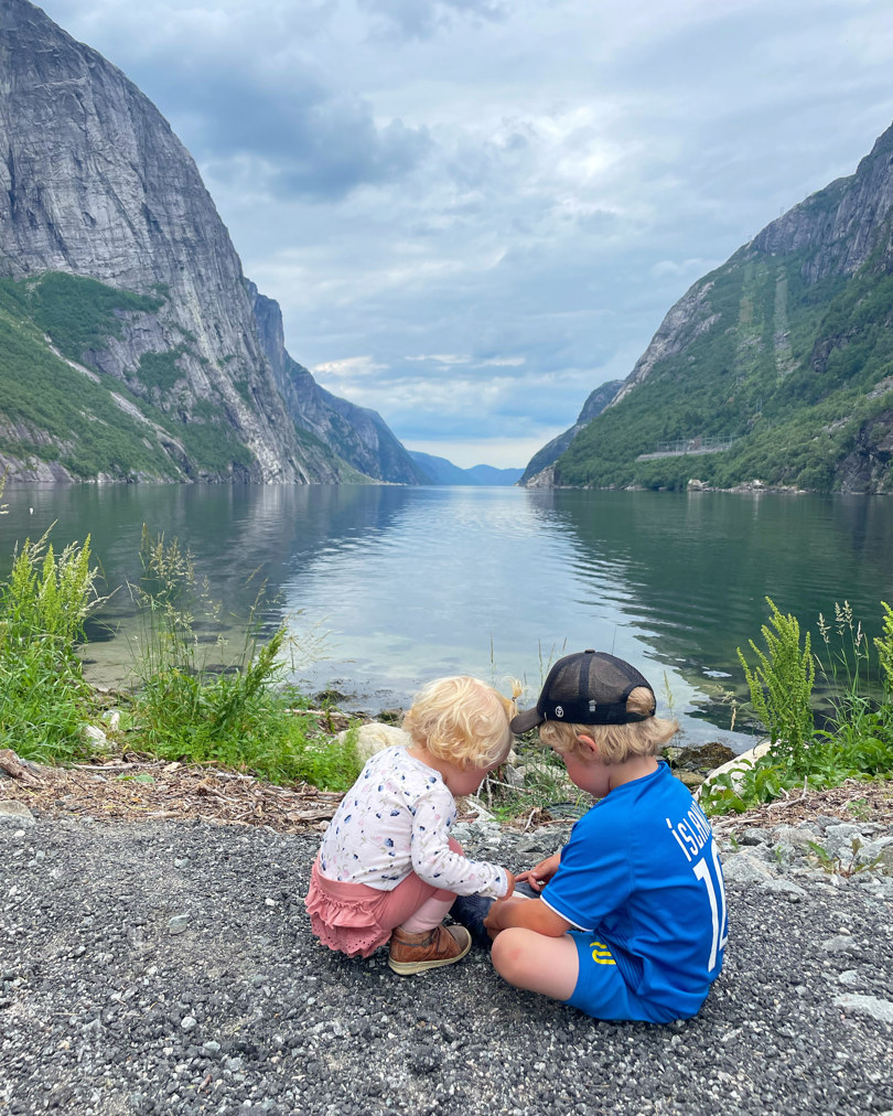 En gutt og en jente leker i sanden like ved en fjord.