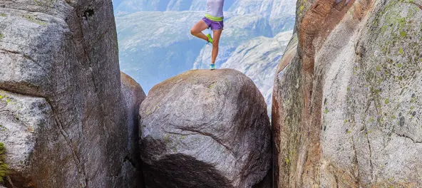 En jente står på et ben på en stein som er kilt fast mellom to fjellsider.
