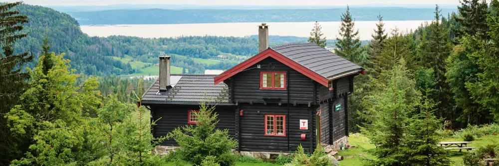 Svartmalt hytte med røde karmer med utsikt mot en fjord