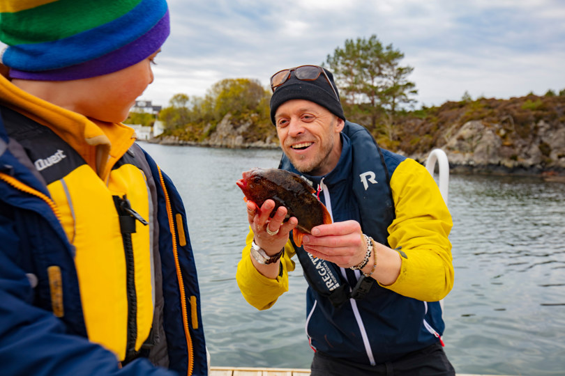 Mann viser frem fisk til gutt, ved sjøen.