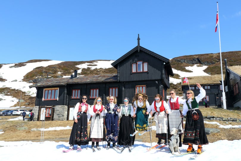 bunadskledde damer med ski på beina foran turisthytte