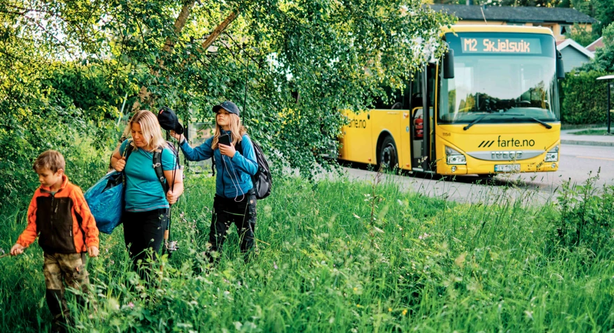 Tre turgåere i grønne omgivelser, buss i bakgrunnen
