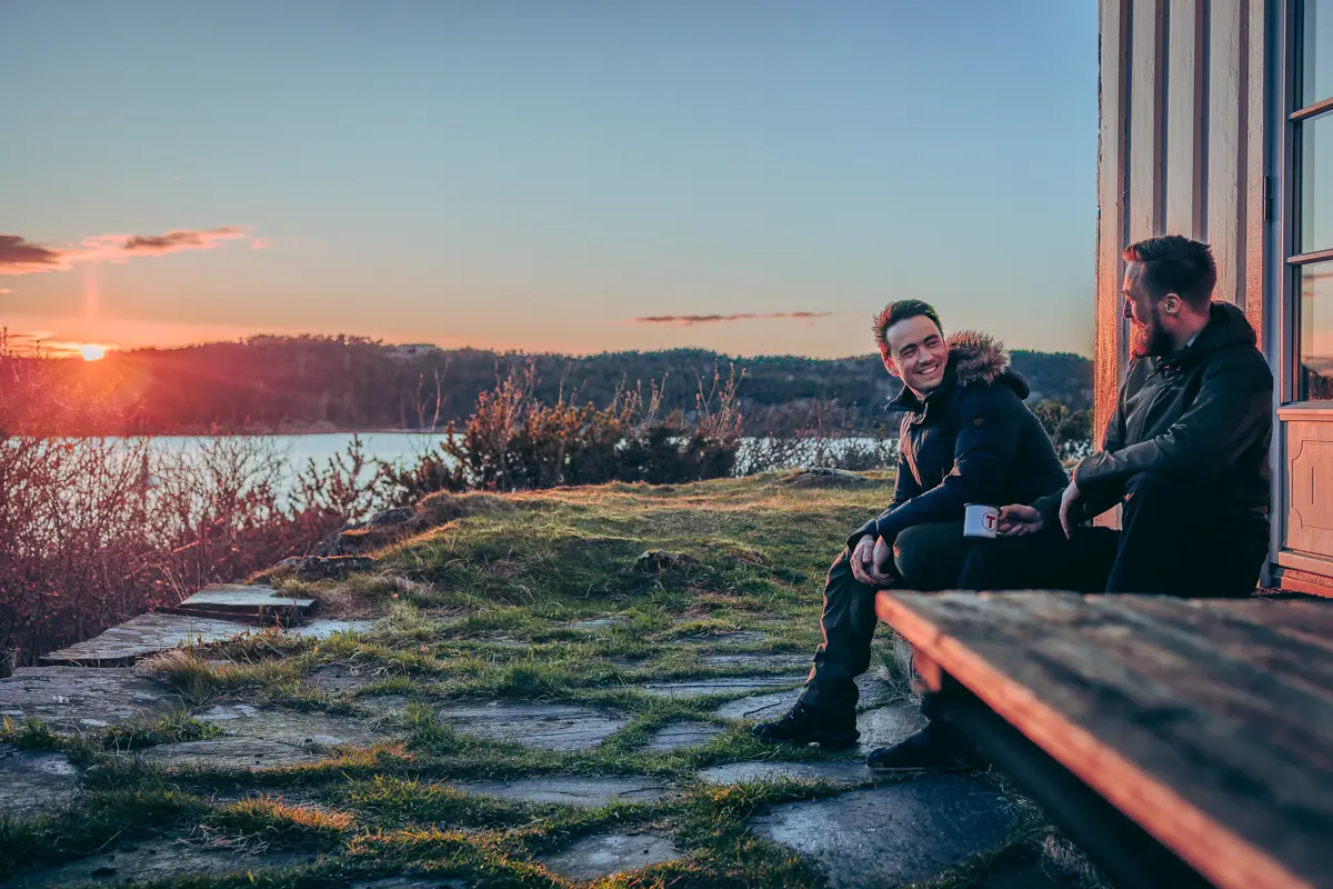 To venner som sitter i solnedgangen på Gammeløya med en kopp kaffe.