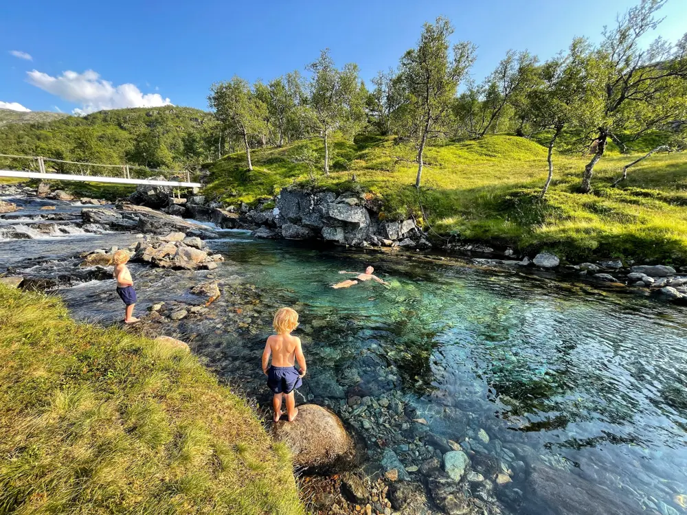 Mann bader i elv, to barn ser på