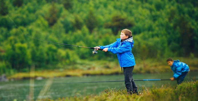 En gutt i blå jakke som kaster sluk med fiskestanga