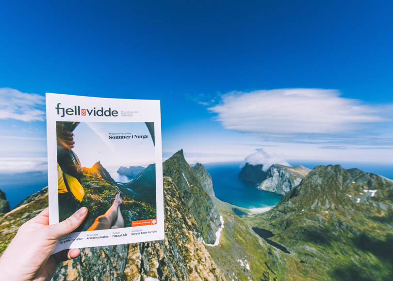 en hånd som holder en bok foran en fjellkjede
