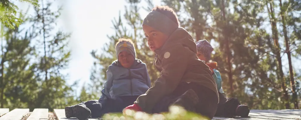 Tre barn som sitter på bakken i skogen