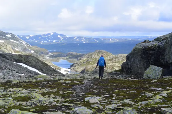 En person med blå ryggsekk går innover et skar med stein og mose, med flotte fjell i horrisonten.