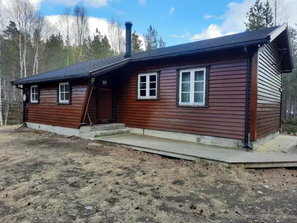 Rød hytte med platt foran og blå himmel i bakgrunnen.
