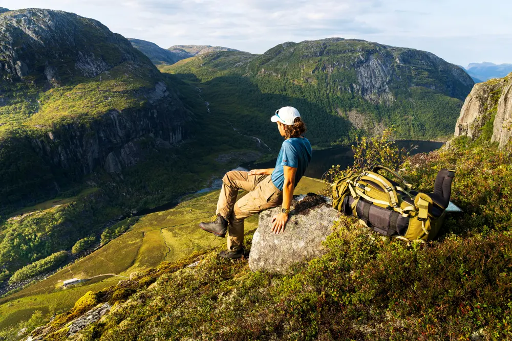 Mann sitter på stein med utsikt mot dal bak