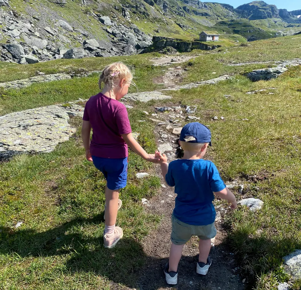 Et liten jente og en liten gutt holder hender og går tur i fjellet.