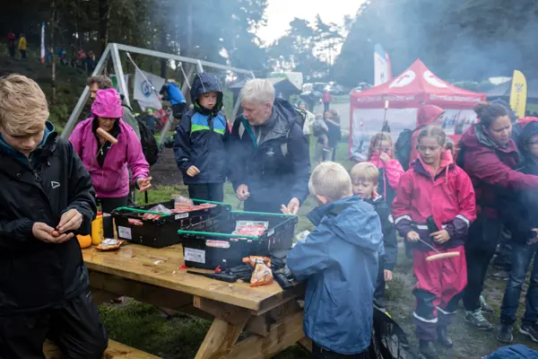 Barn og voksne griller pølser på grillpanne.