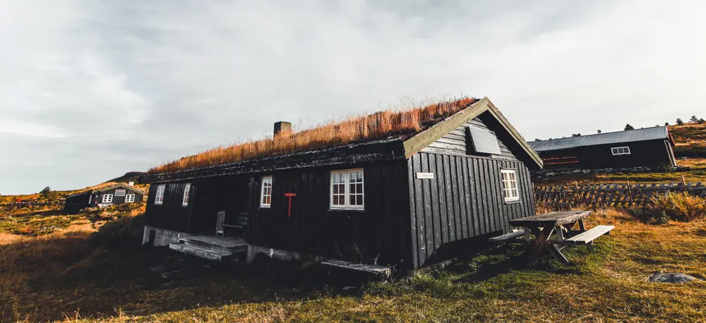 Svartmalt hytte med torvtak og en stor t på veggen.