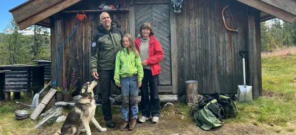 Tre mennesker og en hund foran en hytte