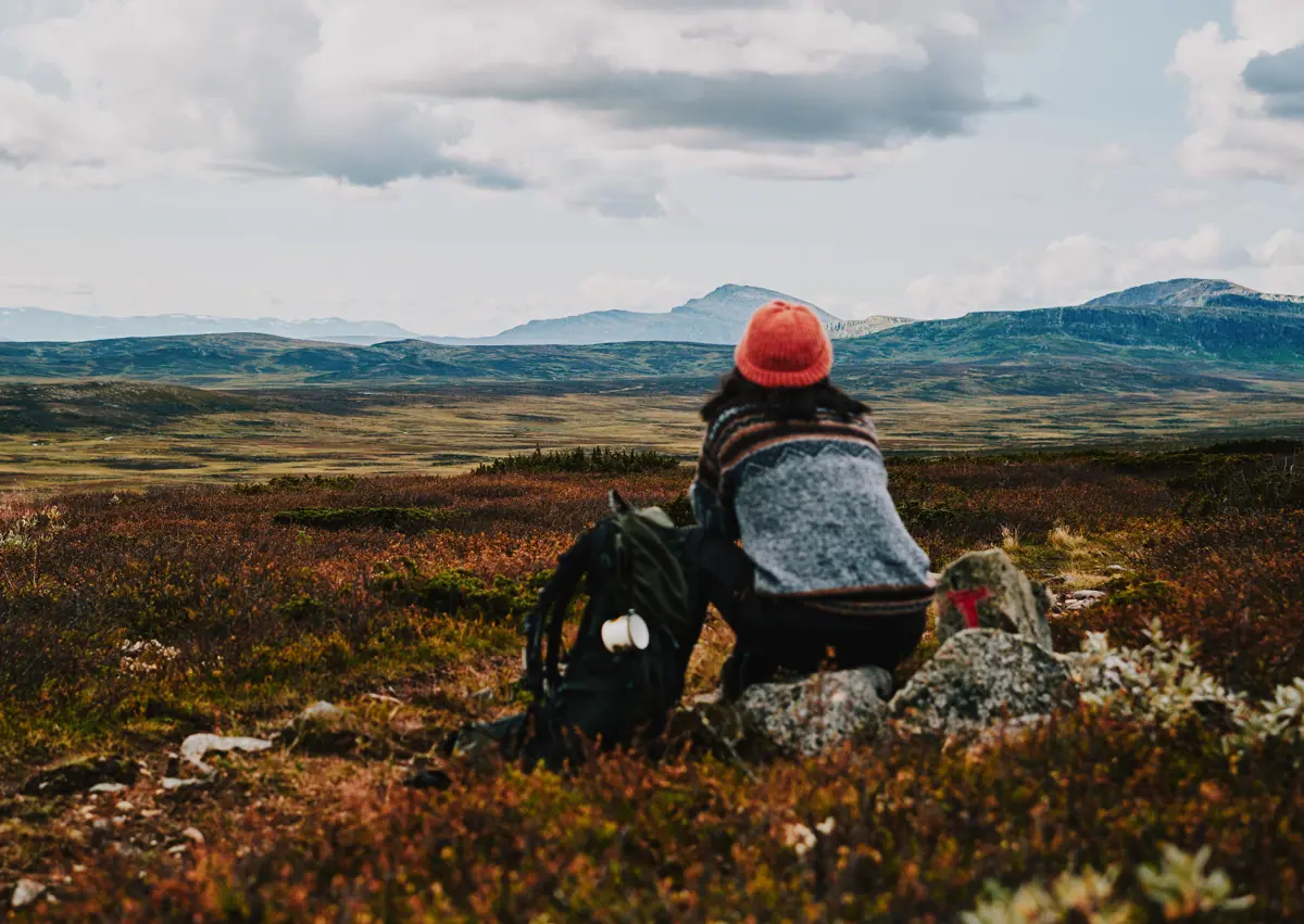 Dame med oransje lue som ser utover et fjellandskap