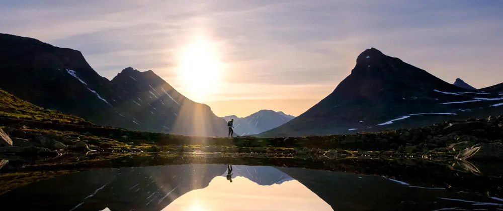 Person som går i fjellet med solnedgang i bakgrunnen