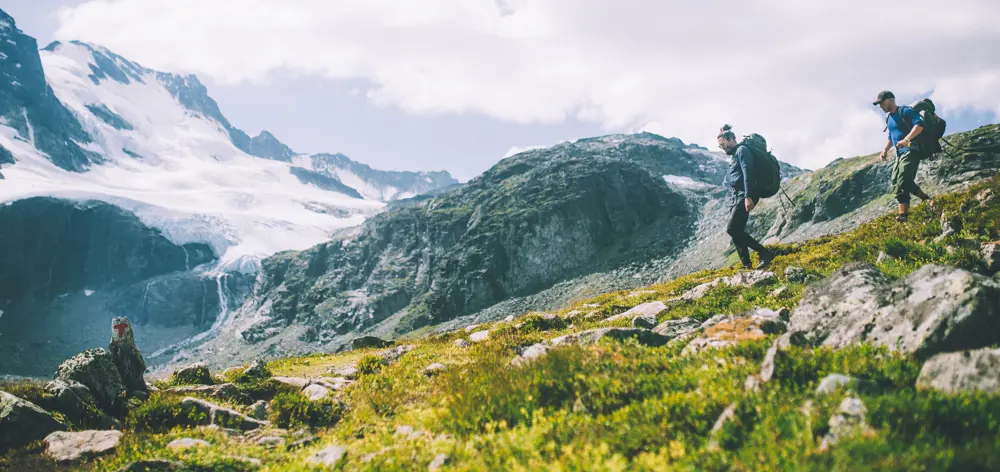 To menn går i flott fjellandskap. Sommer.