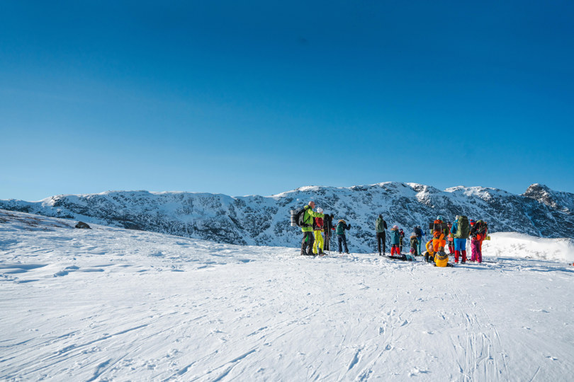 Flere personer med fjellski som stå på en vinterkledd fjelltopp