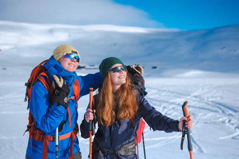 To jenter klare for skitur ser opp mot solen og nyter