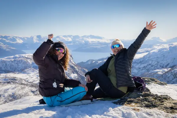 To damer på fjelltopp om vinteren vinker og smiler til kamera.