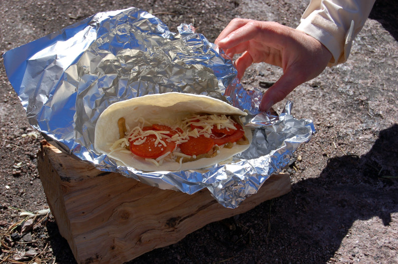 En tacolefse med tomat og ost på, pakkes inn i folie.