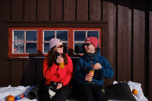 To personer sitter i hyttevegg på vinteren.