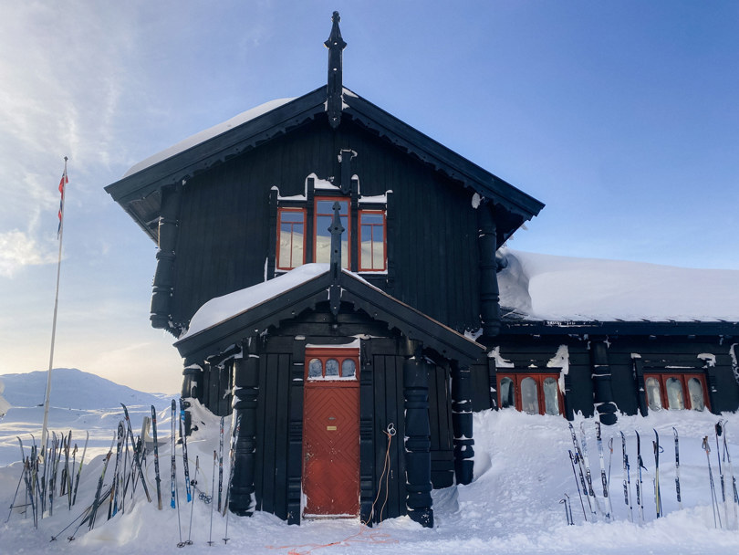Nansensalen på Haukeliseter fjellstue, gammelt tårnbygg i mørkt treverk med mange ski utenfor inngangen av en rødmalt dør