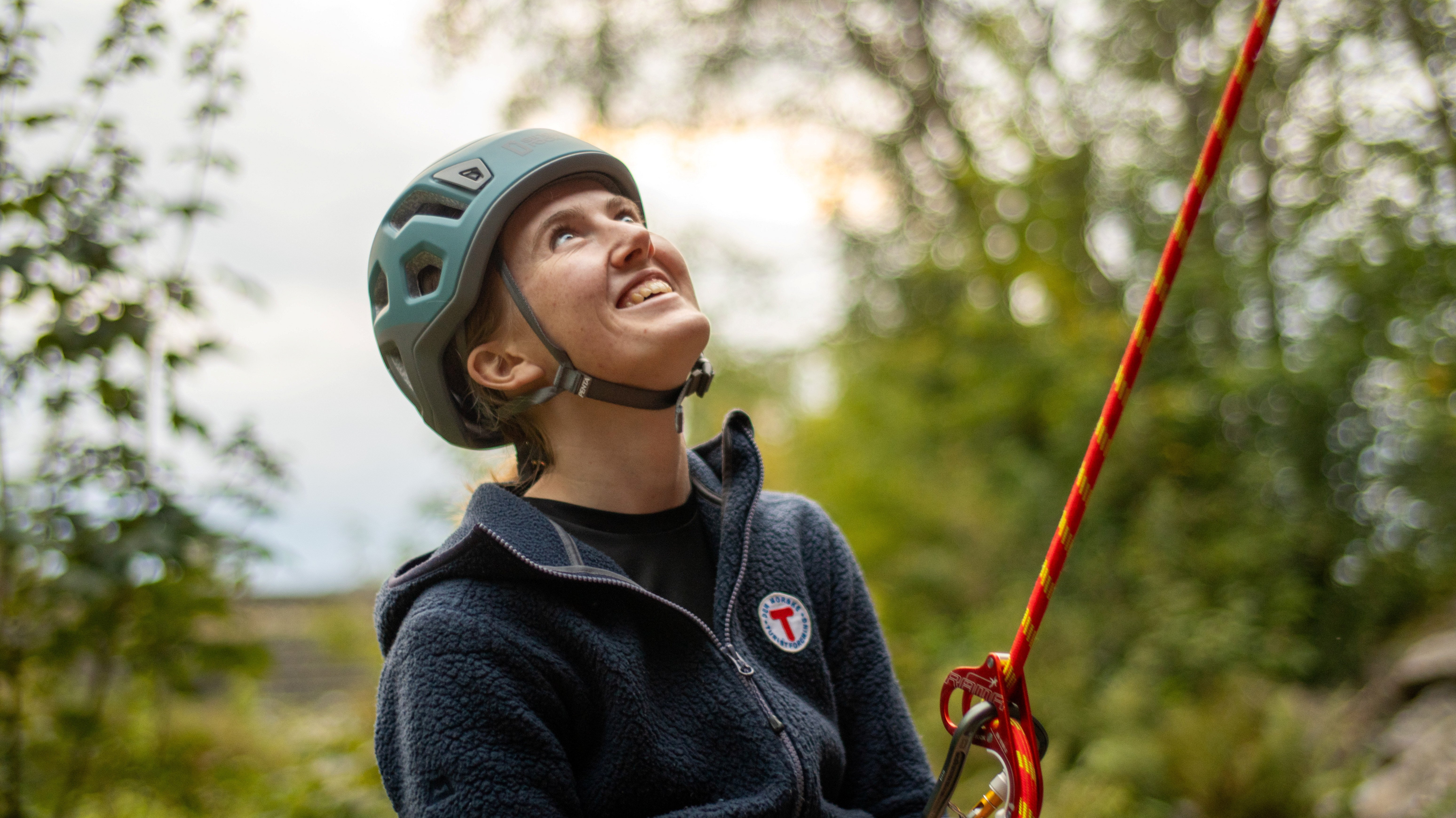 Kvinne med hjelm og tau smiler og ser oppover.