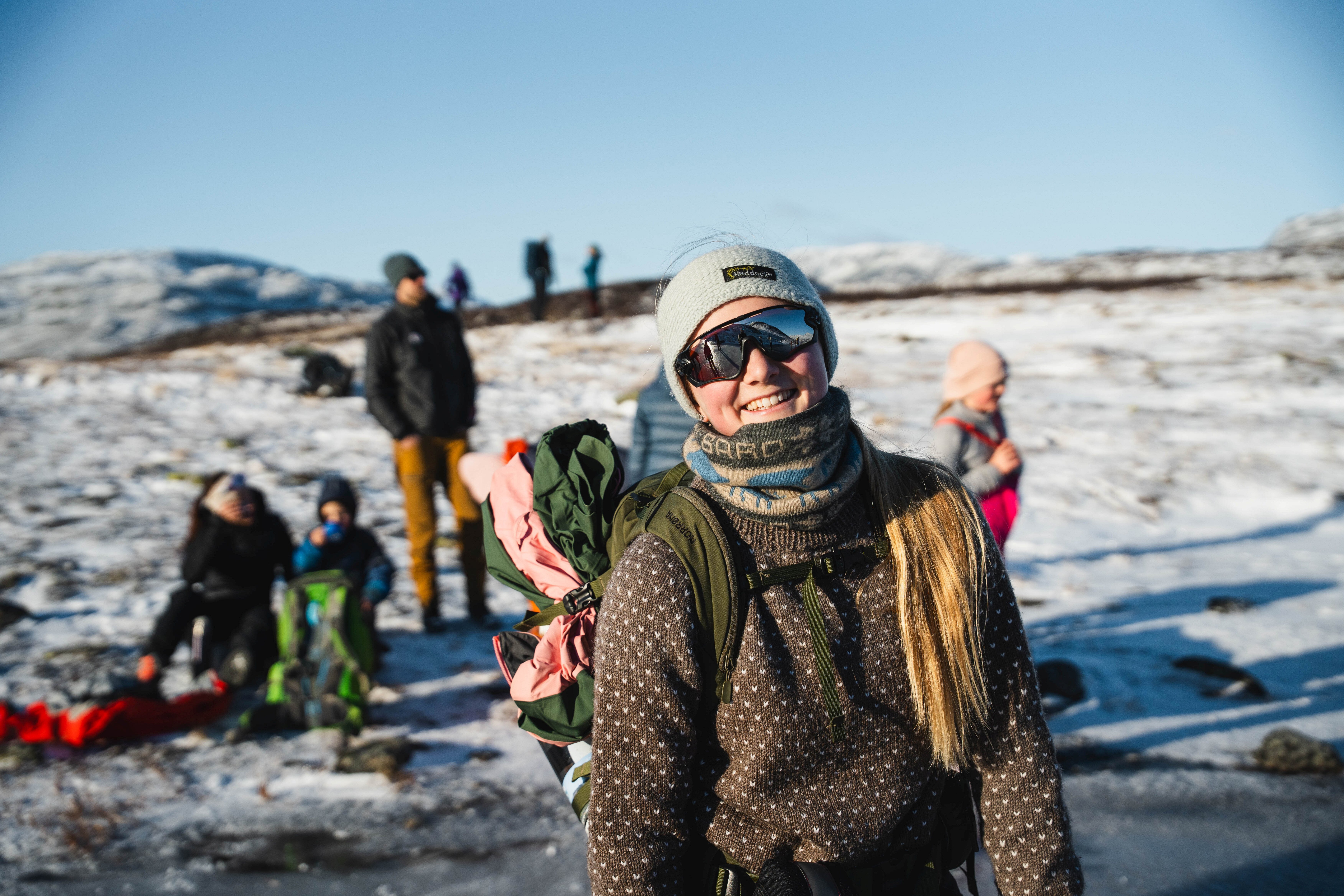 En jente med solbriller står og smiler til kamera.