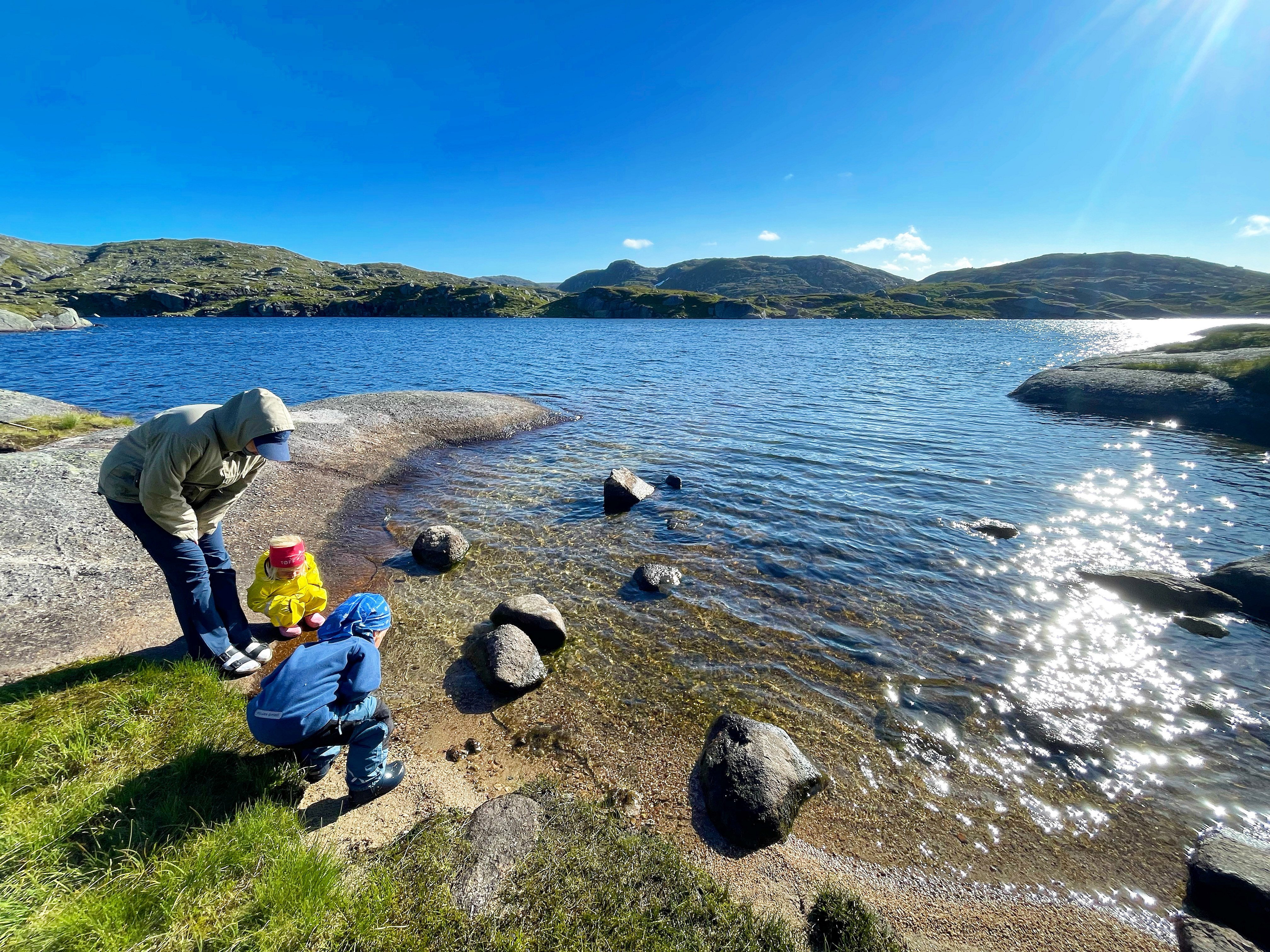 Familie leker på sandstrand ved fjellvann.