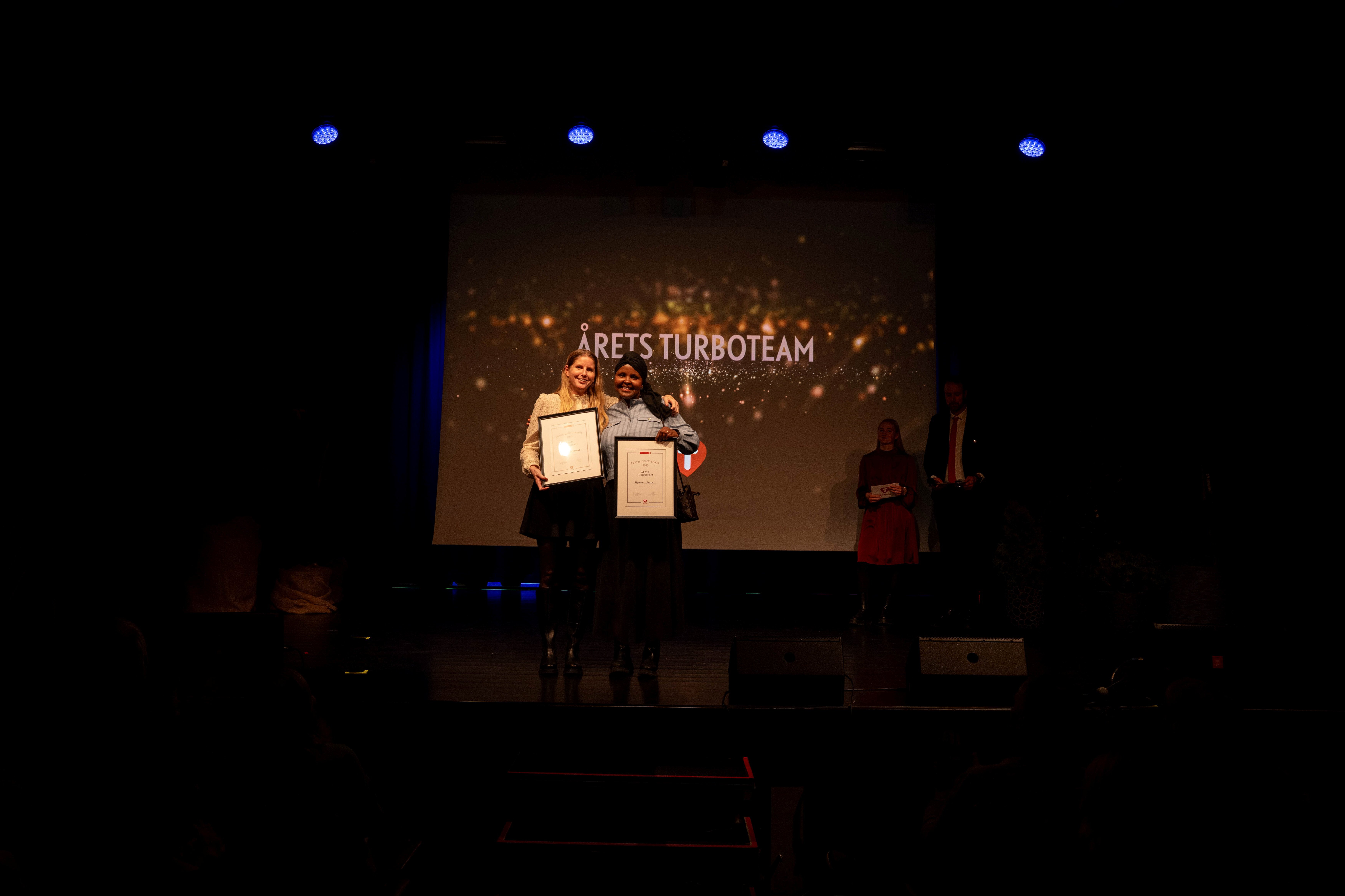 To damer står på en scene og holder fram en pris.