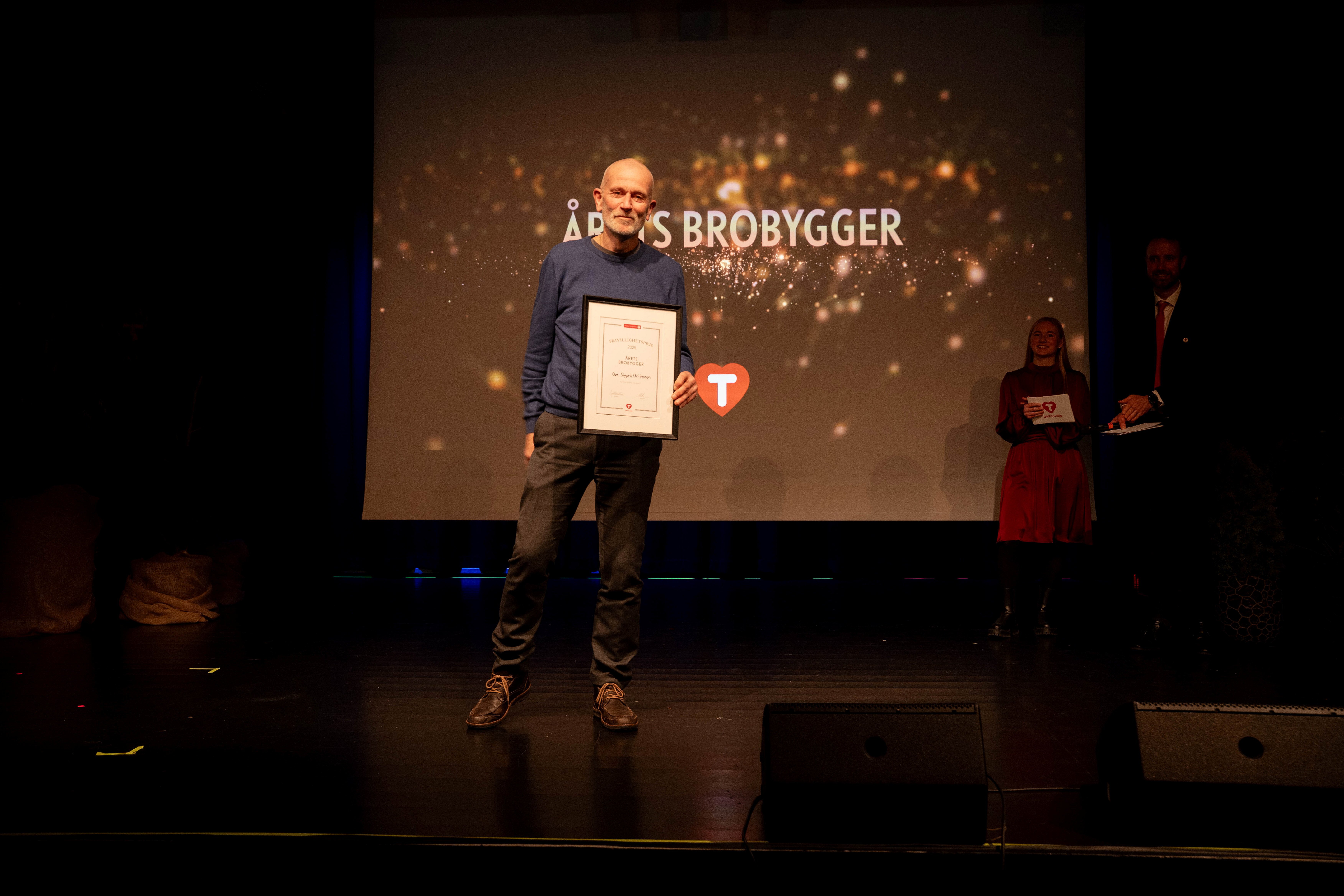 En mann står på en scene og holder fram en ramme med en diplom.