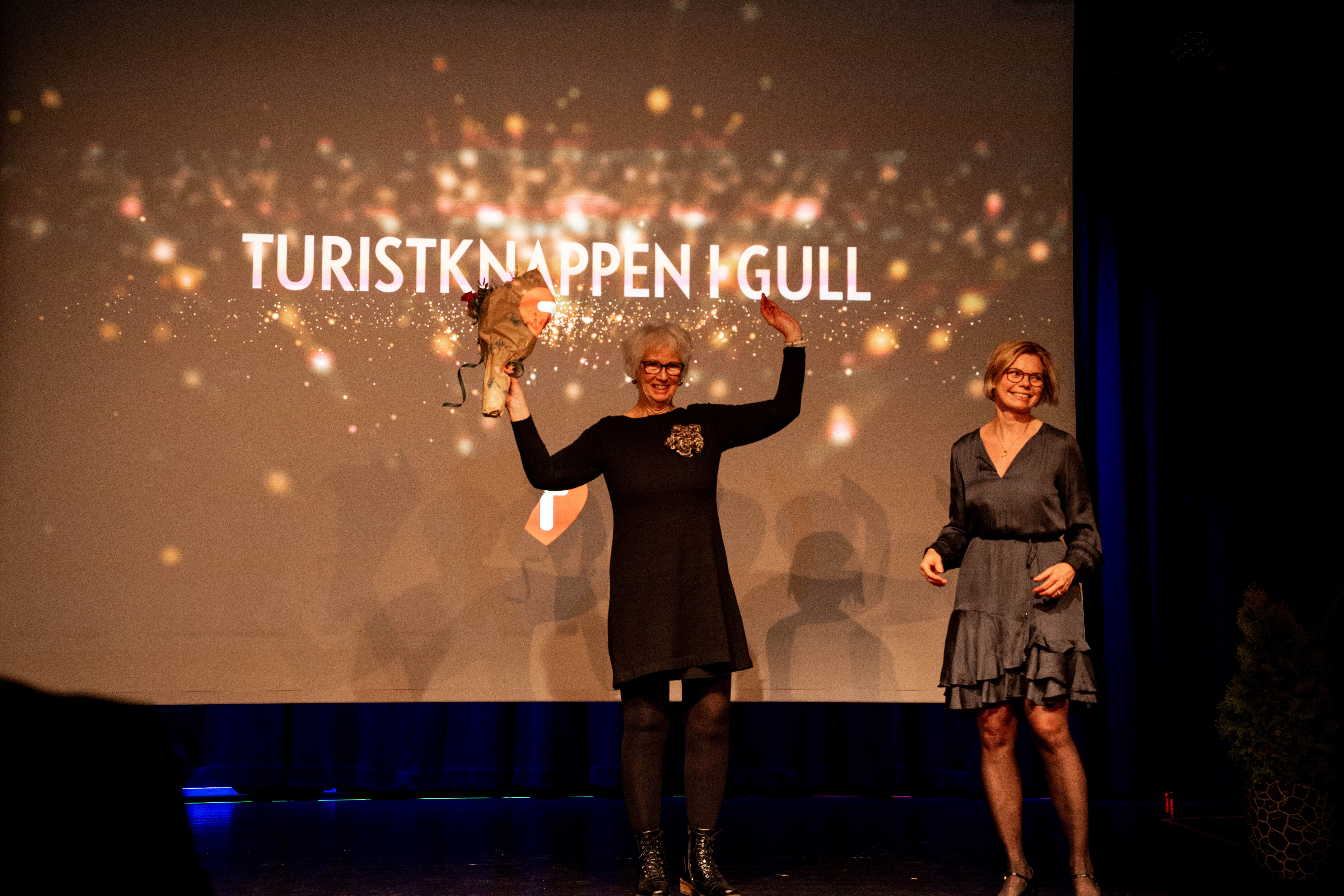 En dame står på en scene og strekker armene i været. Hun har vunnet Turistknappen i gull.