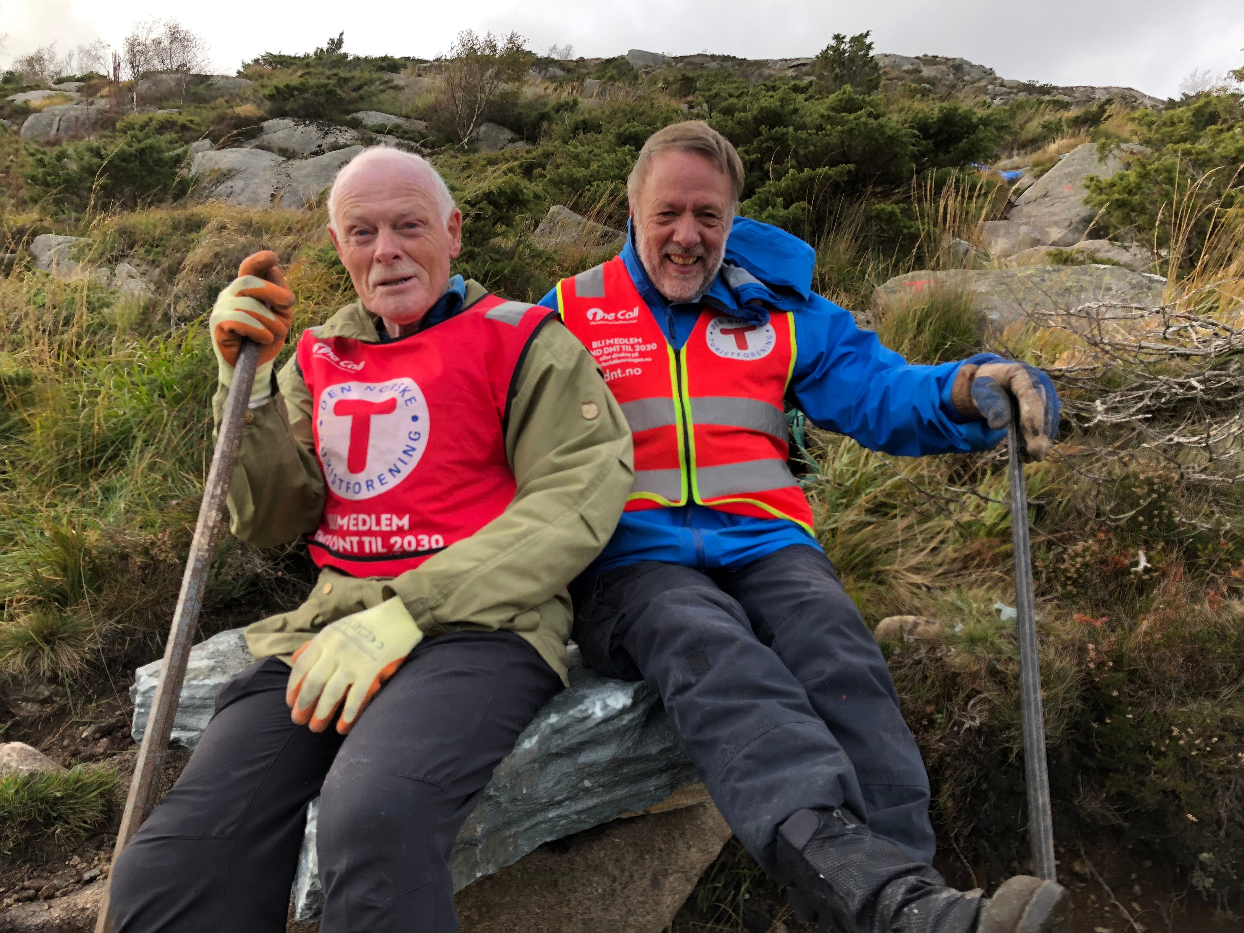 To personer med T-vest sitter og holder en spett i hånda.