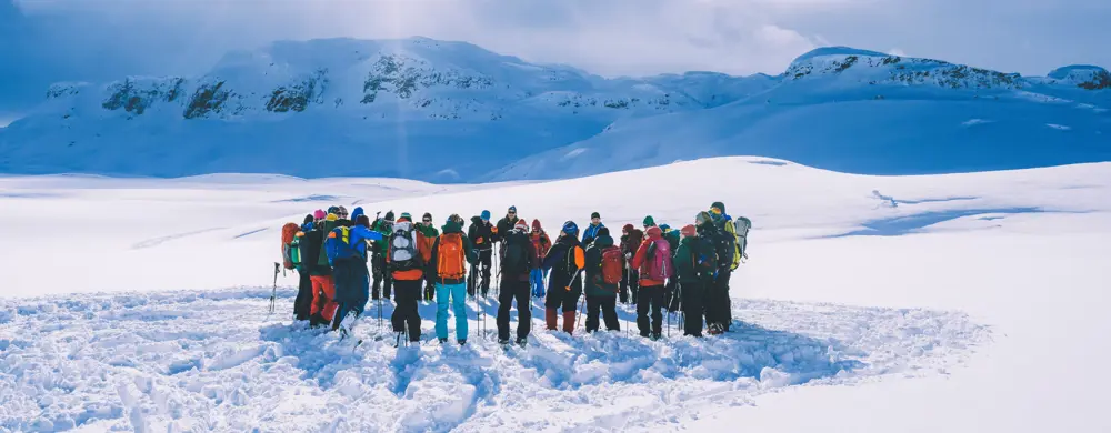 En stor gruppe mennesker som står i ring i vinterfjellet. 
