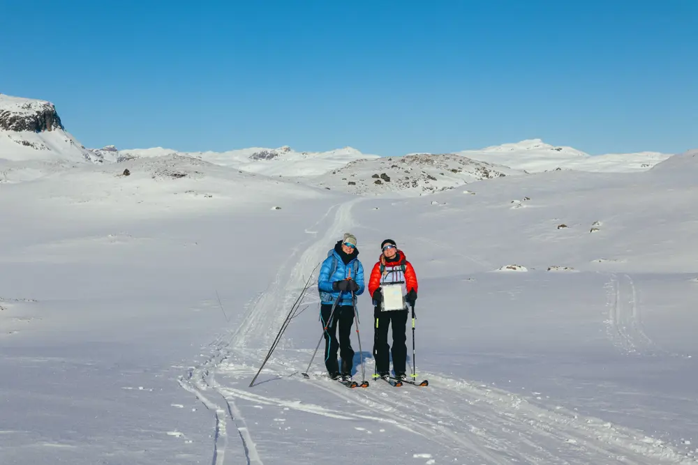 To personer går på ski i et stort landskap dekket av snø. 