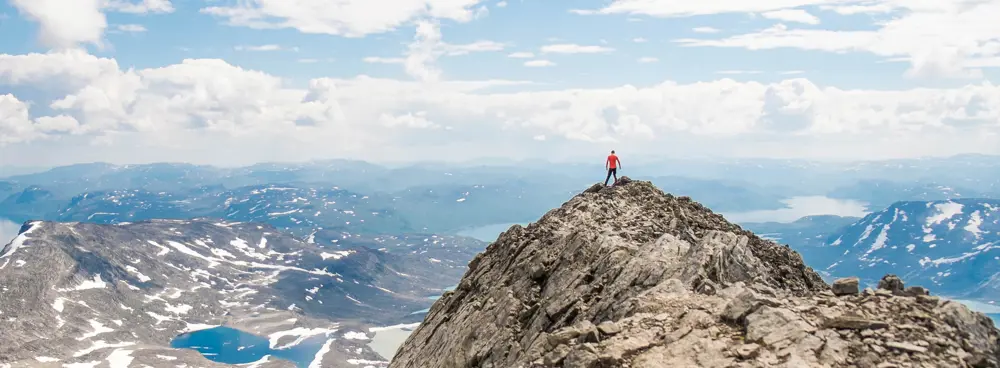 Mann som står på toppen av en fjelltopp og ser utover. 