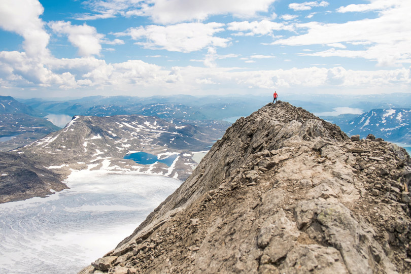 Mann som står ytterst på en fjelltopp