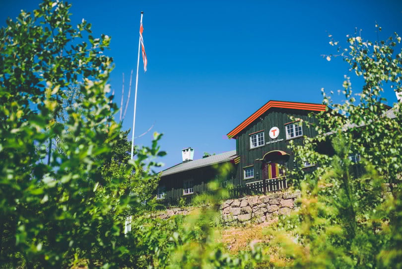 En svartmalt hytte med rød karmer i solskinn