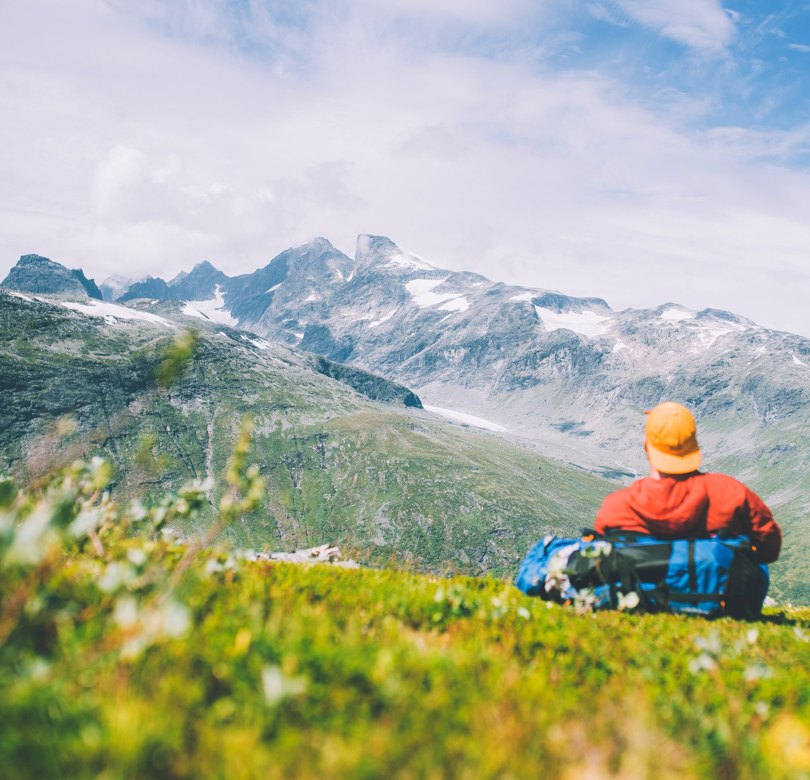En person med caps som ligger i fjellet og ser mot noen fjelltopper