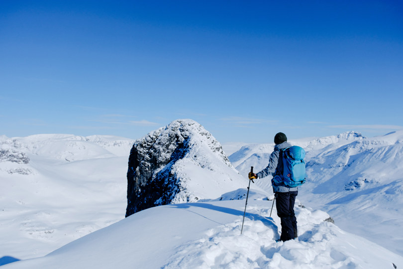 En person med skiutstyr som står og ser utover vinterfjellet