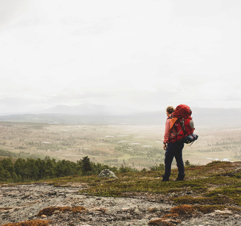 En person med rød sekk som ser utover fjellandskap