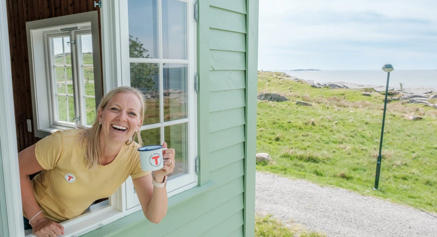 Kvinne smiler i et vindu og holder en kaffekopp