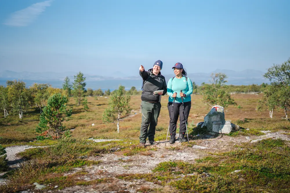 To personer som ser dit mannen peker. De står i et fjellområde, det er blå himmel