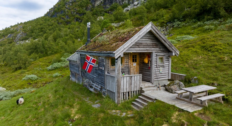 Koselig klassisk hytte med torvtak og norsk flagg utenfor.