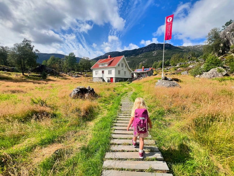 Jente går på sti mot hvit hytte