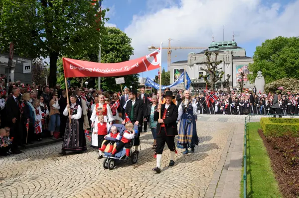 Turlagsmedlemme i 17. mai tog i Bergen med sol foran Den Nasjonale Scene.