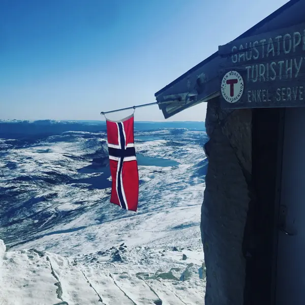 en hytte på toppen av et fjell med et norsk flagg utenfor døra