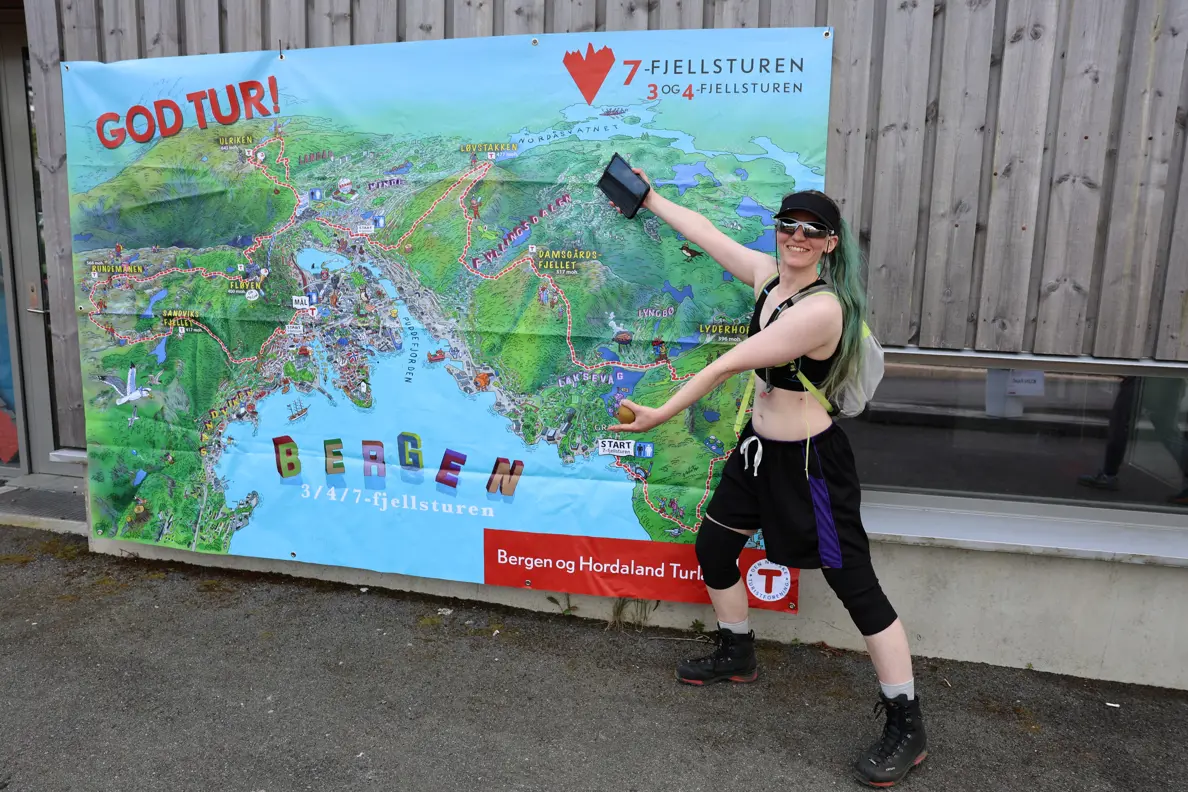 Dame med shorts, solbriller og caps viser frem ruten på 7-fjellsturen.