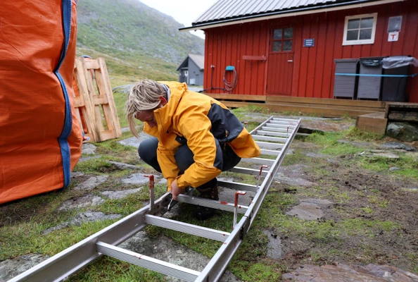 Person jobber med en stige foran hytte.
